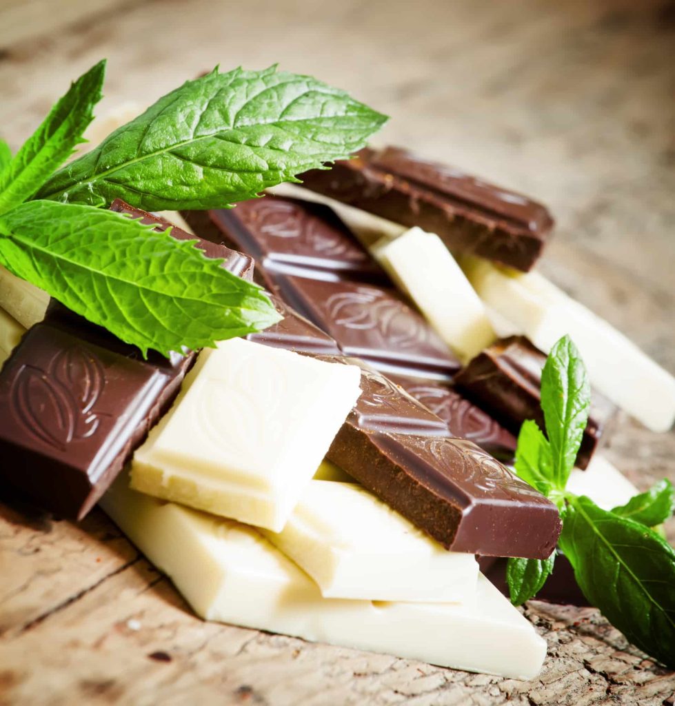 A small pile of milk and white cannabis chocolate on a table with mint leaves.